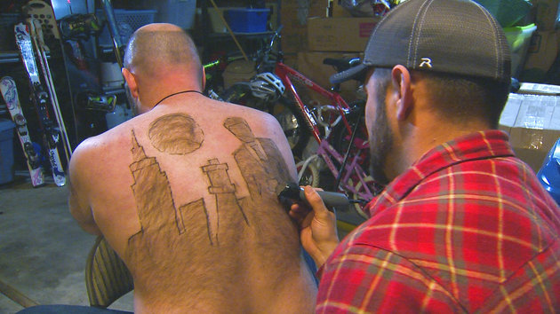 CORRECTS DATE TO DEC. 29 FROM DEC. 30 - In this Dec. 29, 2015 photo provided by KTVB-TV, Tyler Harding, right, trims a design on Mike Wolfe out of his back hair in Nampa, Idaho. Wolfe and Harding meet up several times throughout the year to design a new creation on Wolfes back. The designs have since been compiled for a calendar. (Mike di Donato/KTVB via AP) TV OUT, MANDATORY CREDIT