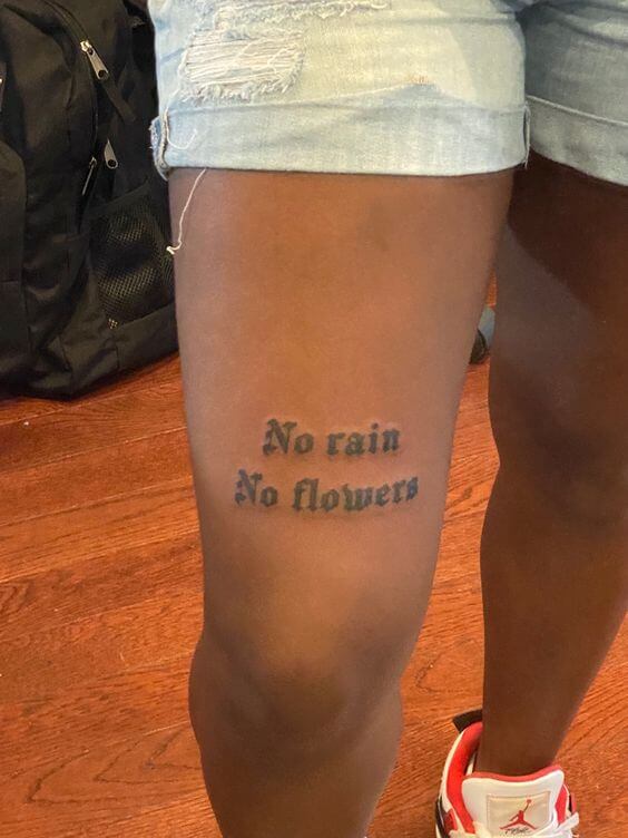 above knee tattoo of the words no rain no flowers 